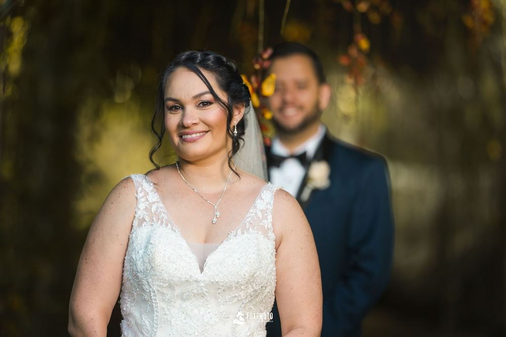 Novia sonriendo con el novio detrás bajo luz cálida