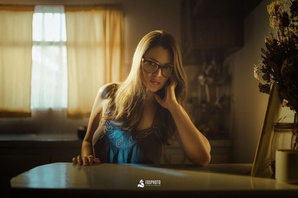 Mujer con lentes junto a una ventana con luz cálida