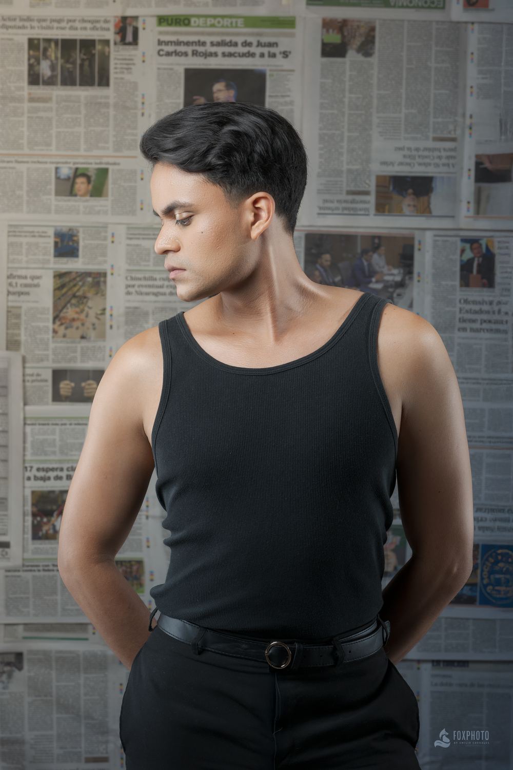 Retrato de hombre con camiseta negra frente a una pared de periódicos