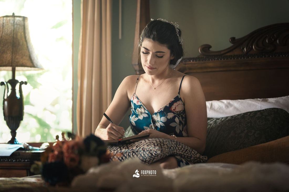 Novia sentada en la cama escribiendo en su diario la mañana de su boda